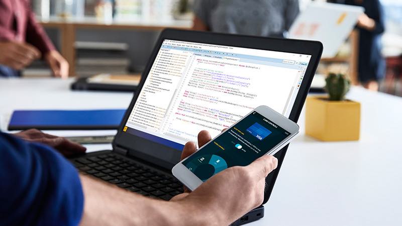 Developer in office environment with open laptop looking at smart phone. Developer in office environment with open laptop looking at smart phone.