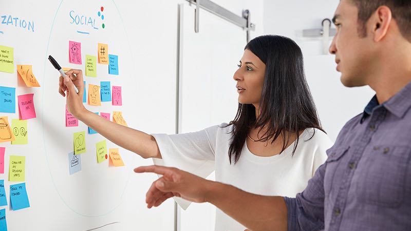 Man and woman brainstorming at Scrum task board. Man and woman brainstorming at Scrum task board.