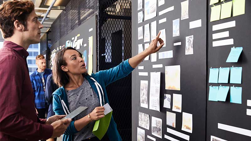 Mujer haciendo una indicación sobre un pizarron a un colaborador