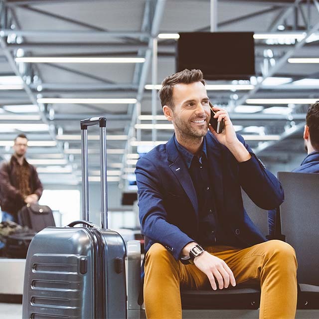 Hombre sonriente hablando por teléfono en un aeropuerto
